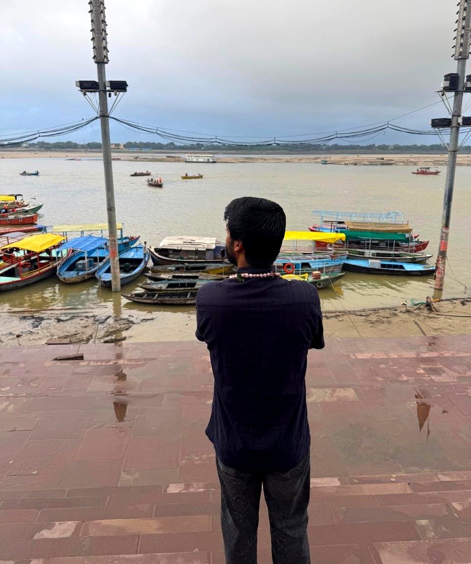 A solo traveler looking out at the Ganga and boats from a ghat in Varanasi